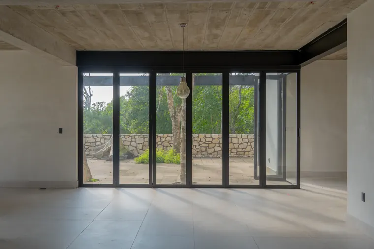 Estancia con cancel plegable de piso a techo hacia el patio arbolado