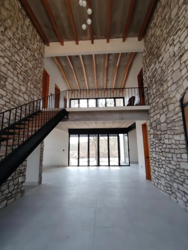 Estancia a doble altura con muros de piedra, vigas de madera y escalera de herrería