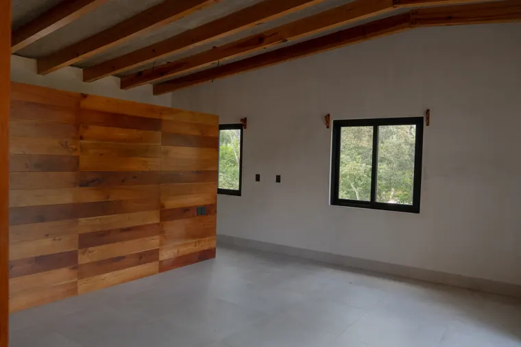 Recámara con muro de madera, vigas aparentes y ventanas al bosque