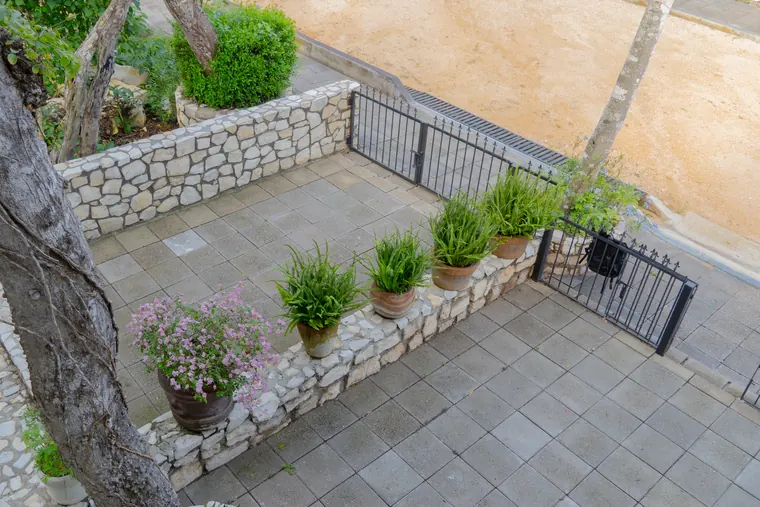 Patio de acceso con muros de piedra, helechos y buganvilias